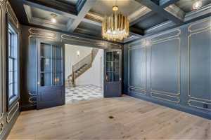 Interior space featuring light wood-type flooring, an inviting chandelier, crown molding, and coffered ceiling