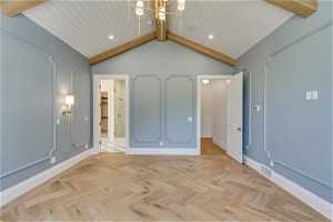 Unfurnished bedroom featuring vaulted ceiling with beams, light parquet flooring, and a chandelier