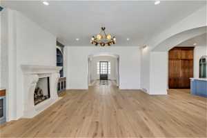 Unfurnished living room featuring built in features, light hardwood / wood-style flooring, a brick fireplace, and an inviting chandelier