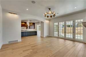 Unfurnished living room featuring light hardwood / wood-style flooring, french doors, and an inviting chandelier