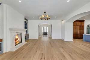 Unfurnished living room featuring light hardwood / wood-style flooring, a chandelier, built in features, and a brick fireplace