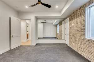 Interior space with light colored carpet, ceiling fan, and brick wall