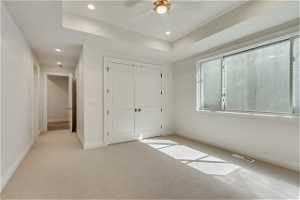 Unfurnished bedroom featuring a closet, a raised ceiling, ceiling fan, and light carpet