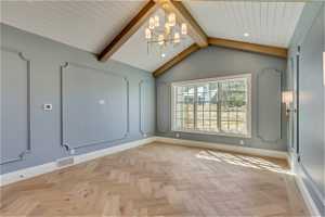 Spare room featuring vaulted ceiling with beams, a notable chandelier, and light parquet flooring