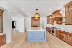 Kitchen featuring decorative light fixtures, backsplash, range with two ovens, light hardwood / wood-style floors, and an island with sink
