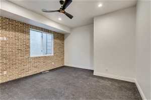 Carpeted empty room featuring brick wall and ceiling fan