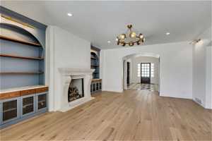 Unfurnished living room with built in features, light hardwood / wood-style floors, a brick fireplace, and a notable chandelier