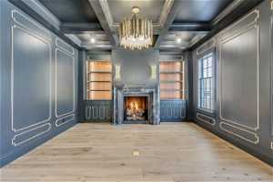 Unfurnished living room featuring a premium fireplace, coffered ceiling, a notable chandelier, light wood-type flooring, and crown molding