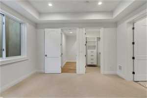 Unfurnished bedroom featuring a closet, a spacious closet, a raised ceiling, and light carpet