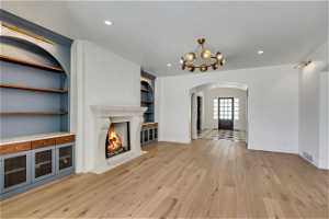 Unfurnished living room with built in shelves, an inviting chandelier, light hardwood / wood-style flooring, and a fireplace
