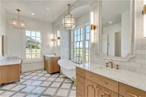 Bathroom featuring dual bowl vanity, a bath to relax in, tile flooring, a notable chandelier, and tasteful backsplash