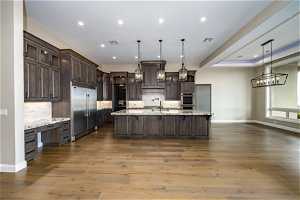 Kitchen featuring hardwood / wood-style floors, stainless steel appliances, tasteful backsplash, dark brown cabinetry, and an island with sink