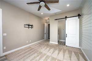 Unfurnished bedroom with light carpet, ceiling fan, and a barn door