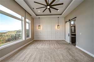 Spare room featuring ceiling fan, a tray ceiling, light carpet, and a barn door
