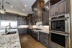 Kitchen with appliances with stainless steel finishes, wood-type flooring, tasteful backsplash, and light stone counters