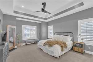 Bedroom featuring light colored carpet, ceiling fan, and a tray ceiling