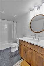 Full bathroom with tile flooring, tile walls, shower / tub combo with curtain, toilet, and vanity