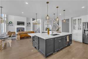 Kitchen featuring pendant lighting, white cabinets, a fireplace, stainless steel refrigerator, and light hardwood / wood-style floors