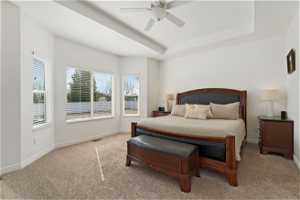 Carpeted bedroom featuring ceiling fan and a tray ceiling