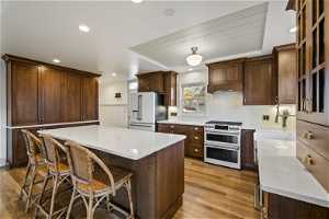 Kitchen with high end appliances, a breakfast bar, white oak hardwood flooring, backsplash, and a kitchen island