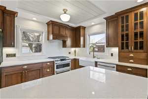 Kitchen with range with two ovens, backsplash, light stone counters, sink, and stainless steel dishwasher