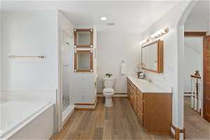 Primary suite bathroom with vanity, separate shower, jetted tub, toilet, and hardwood / wood-style flooring