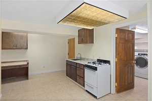 Basement kitchen featuring gas range gas stove, light tile floors, sink, and washer/dryer