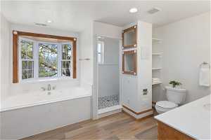 Primary suite bathroom with independent shower and jetted bathtub, vanity, hardwood / wood-style flooring, and toilet