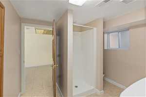 Basement bathroom with walk-in shower, a textured ceiling, and tile flooring