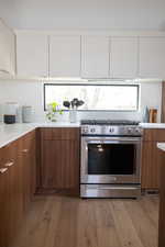 Kitchen with stainless steel stove, wood-type flooring, and white cabinets