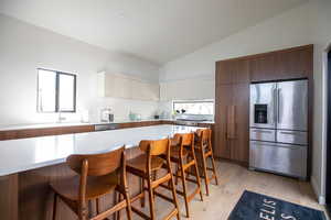 Kitchen with appliances with stainless steel finishes, vaulted ceiling, light hardwood / wood-style floors, white cabinetry, and a kitchen breakfast bar