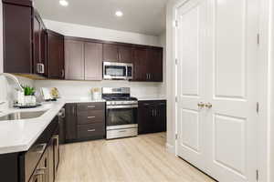 Kitchen featuring a sink, light countertops, appliances with stainless steel finishes, dark brown cabinetry, and light wood-style floors