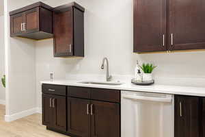 Kitchen with a sink, dark brown cabinets, stainless steel dishwasher, and light countertops