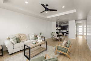 Living area featuring baseboards, a raised ceiling, ceiling fan, recessed lighting, and light wood-style flooring