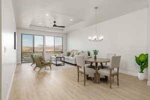 Dining space with a tray ceiling, baseboards, light wood-style floors, and ceiling fan with notable chandelier