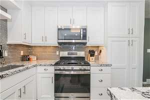 Kitchen with tasteful backsplash, appliances with stainless steel finishes, and white cabinets