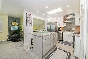 Kitchen with light colored carpet, appliances with stainless steel finishes, white cabinets, a skylight, and a center island