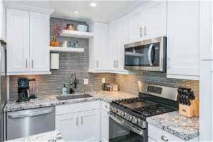 Kitchen with backsplash, stainless steel appliances, white cabinets, and sink