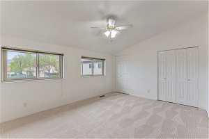 Unfurnished bedroom featuring light colored carpet, ceiling fan, and vaulted ceiling