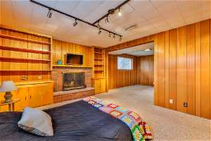 Carpeted bedroom with rail lighting, wood walls, and a fireplace