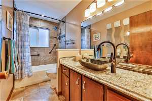 Full bathroom with tile flooring, oversized vanity, toilet, and shower / bath combo with shower curtain