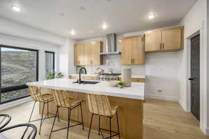 Kitchen featuring light brown cabinetry, wall chimney range hood, sink, stainless steel range oven, and light hardwood / wood-style floors