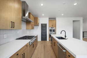 Kitchen with tasteful backsplash, appliances with stainless steel finishes, sink, light wood-type flooring, and wall chimney exhaust hood