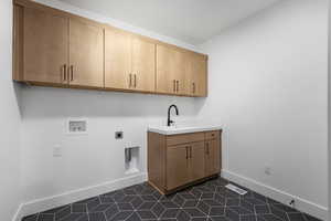 Laundry room with dark tile patterned flooring, hookup for a washing machine, hookup for an electric dryer, sink, and cabinets