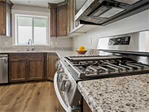 Kitchen with sink, light hardwood / wood-style flooring, stainless steel appliances, and light stone countertops