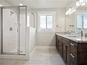 Bathroom with a wealth of natural light, double sink, a shower with shower door, and vanity with extensive cabinet space