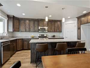 Kitchen with decorative light fixtures, light hardwood / wood-style flooring, stainless steel appliances, and light stone countertops