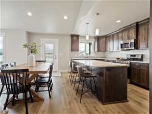 Kitchen with appliances with stainless steel finishes, a kitchen island, hanging light fixtures, light hardwood / wood-style floors, and a kitchen breakfast bar