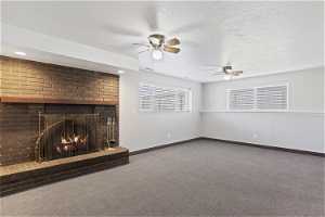 Unfurnished living room with dark colored carpet, a brick fireplace, ceiling fan, and a textured ceiling