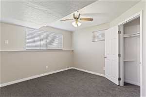 Unfurnished bedroom with a textured ceiling, a closet, ceiling fan, and dark colored carpet